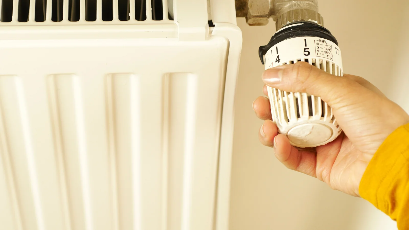 A hand adjusting a thermostatic radiator valve beside a white radiator.