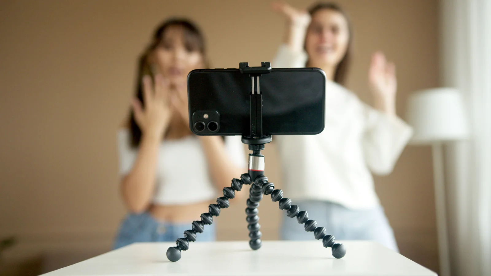 A person using a smartphone on a small support to record video beside a laptop.